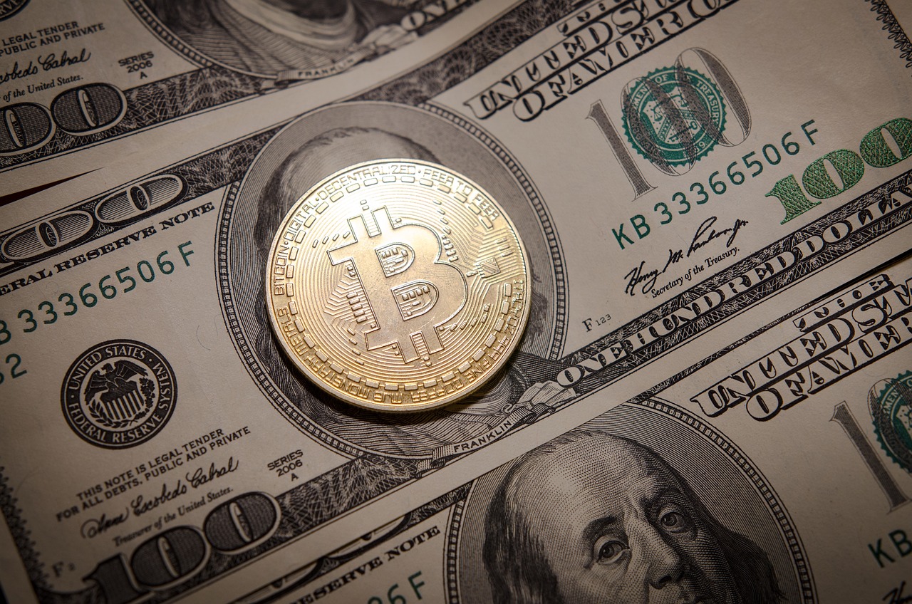 عملة بيتكوين ذهبية موضوعة على أوراق نقدية من فئة 100 دولار أمريكي، ترمز لتأثير البيتكوين على النظام المالي التقليدي.